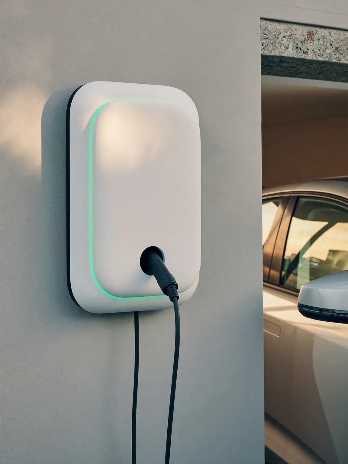 Wallbox branca com anel de luz verde montada na parede de uma garagem, com o cabo ligado a um carro elétrico