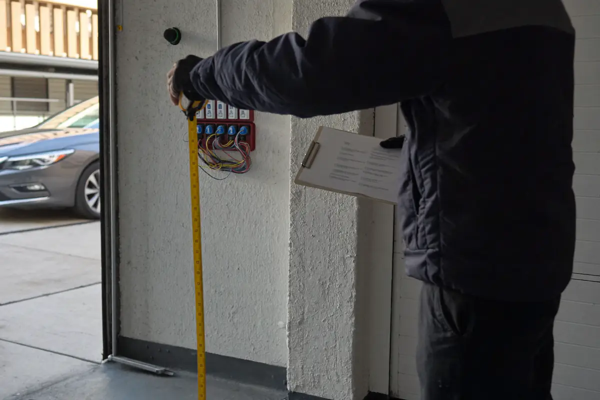 Eletricista a medir com fita métrica a distância ao longo da parede de uma garagem